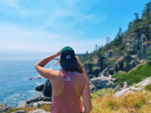 woman looking out over Maine coast wearing green hat with two Maine trees
