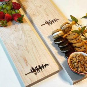 two maple rectangle grazing boards with spruce tree cutouts. One board with fruit, one with cookies